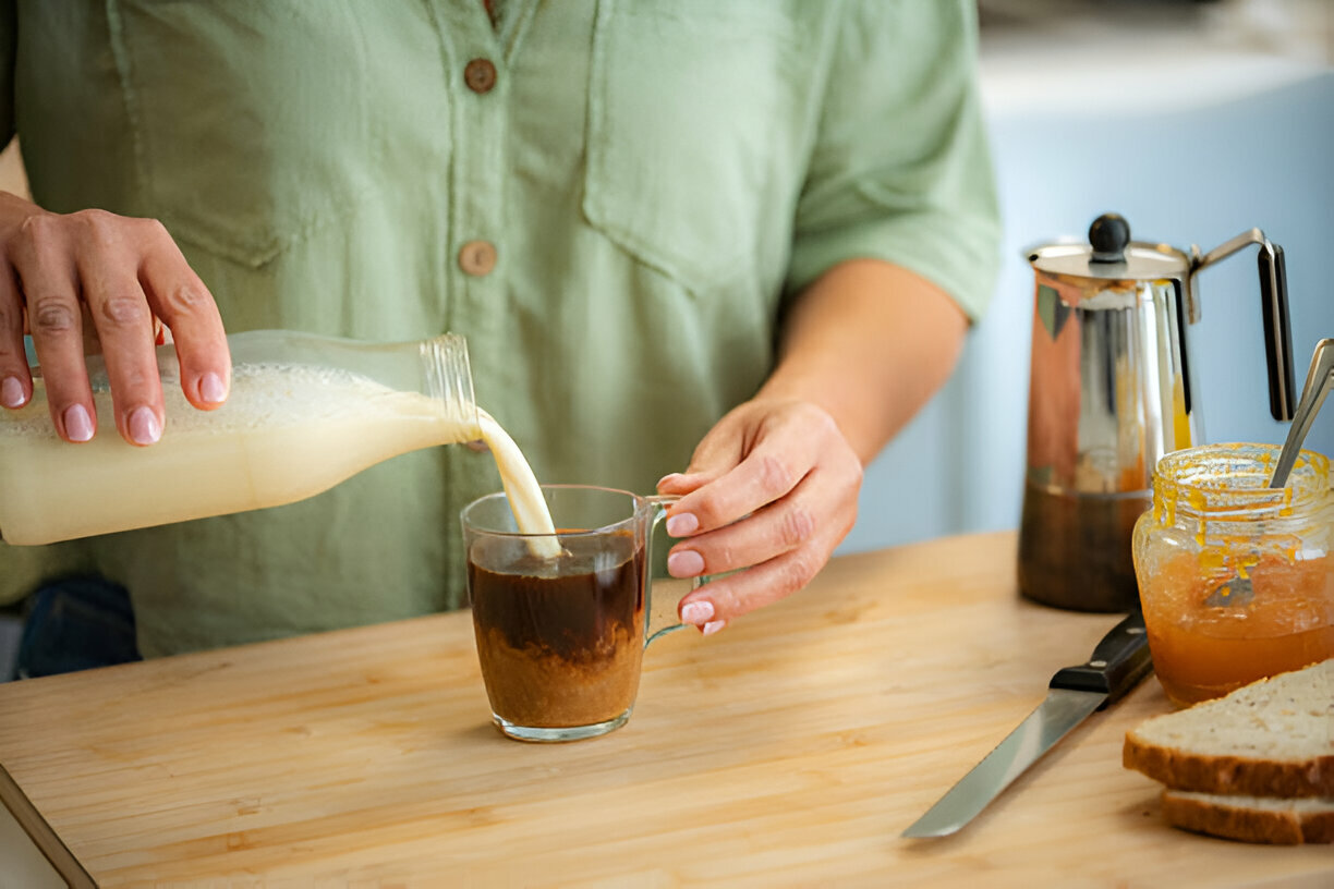 Woman pouring vegan milk into a cup of black coffee. Soy milk, oat milk, almond milk